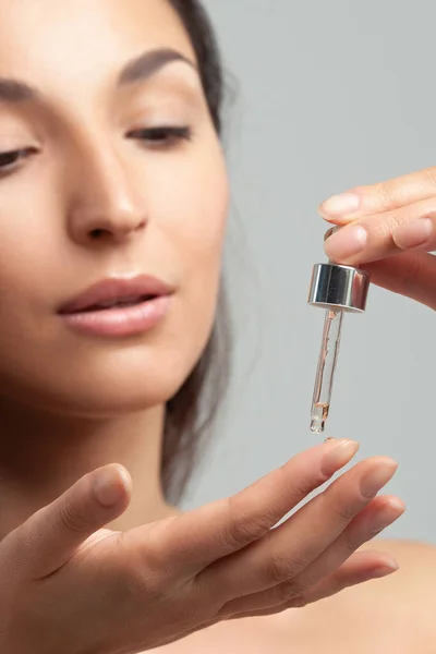 Mükemmel cilde sahip genç ve güzel bir kadın pipette yaşlanmaya duyarlı serum kullanıyor. Cilt bakımı ve yaş kozmetiği