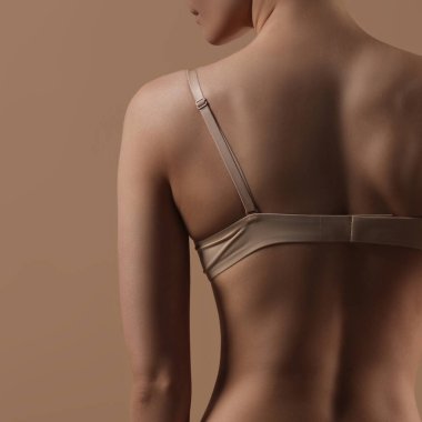 Bej arka planda iç çamaşırlı zayıf bir genç kadın. Arkadan bak. Spor, diyet, cilt ve vücut bakımı