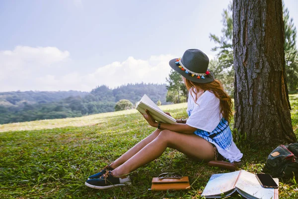 Asyalı kadın doğayı gezer. Seyahat, rahatla. Kız oturmuş ağacın altında kitap okuyor. Sonbahar ormanlarında güzel bir kız kitap okuyor Doğa Eğitimi ve bir not yazıyor..