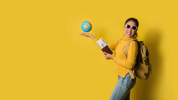 スーツケース付きの女性旅行者,黄色の背景にパスポートとチケットを手にボールグローブを保持. — ストック写真