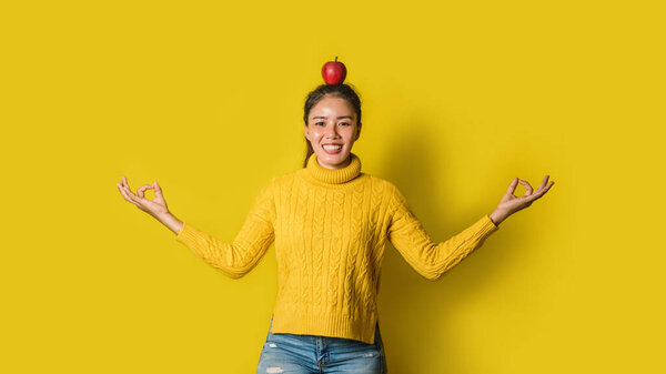 Веселая молодая женщина на жёлтом фоне в студии. Девушка с яблоком на голове во время йоги. Концепция упражнений для хорошего здоровья. Лицензионные Стоковые Изображения