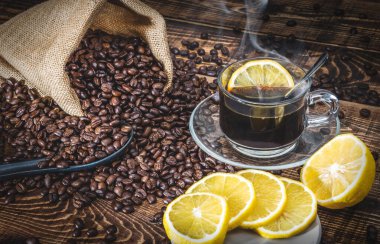 Kahve fincanı ve kavrulmuş kahve çekirdekleri poşette ve ahşap masaya konmuş limon.