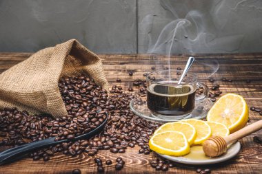 Kahve fincanı ve kavrulmuş kahve çekirdekleri poşette ve ahşap masaya konmuş limon.