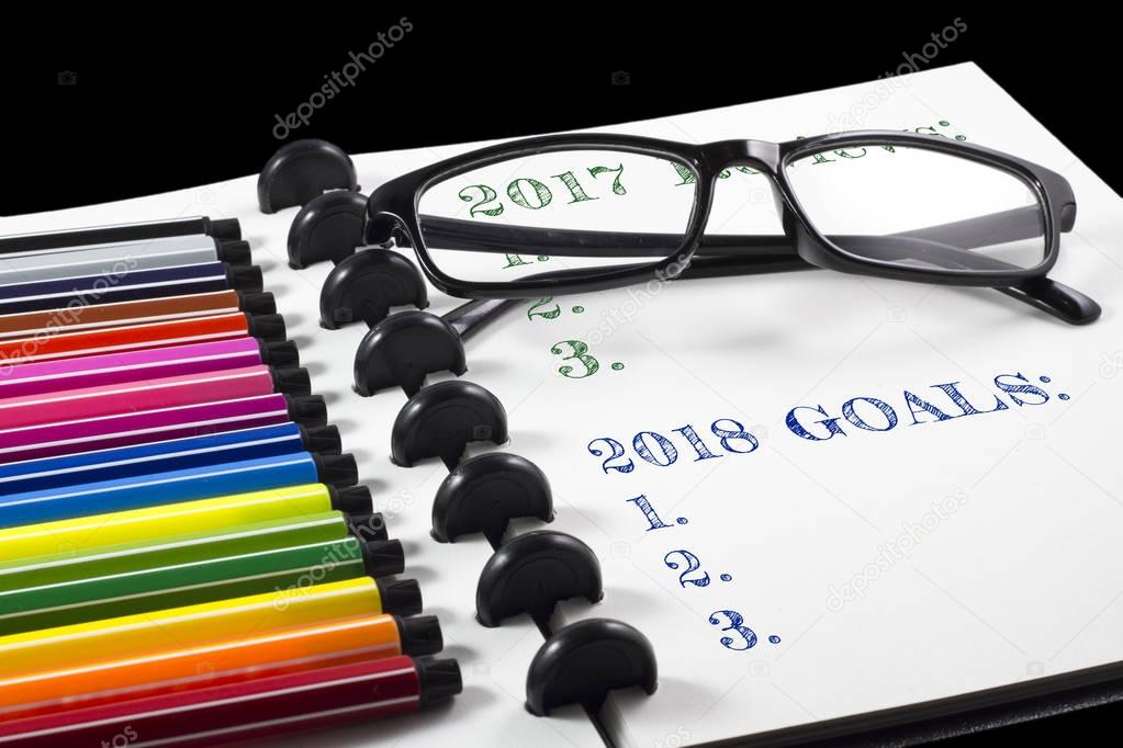 2017 Reviews and 2018 Goals text on white sketchbook with color pen and eye glasses