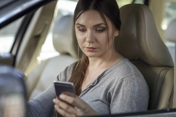Young attractive caucasian woman behind the wheel driving a car with mobile phone in hand in traffic jam. Looking to the screen, danger situation, bad habit. Blue eyes, dard hair, round shape face. Copy space.