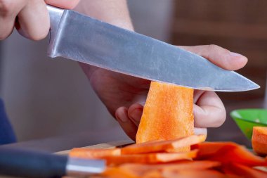 Büyük bıçakla büyük parçalar halinde pişirmek için havuç kesen adam elleri. Sebze mutfağı ya da doğal beslenme malzemeleri. Modern insanın hobisi ya da günlük rutini. Kapalı.