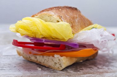 Plastik yiyeceklerle dolu bir sandviçin mecazi görüntüsü.