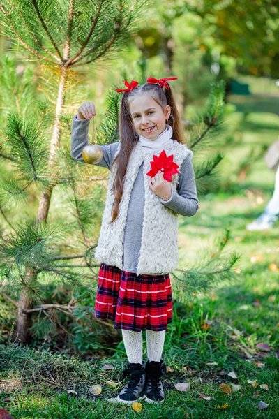 Portrait of a little girl near the Christmas tree. Girl decorates a Christmas tree in the forest with Christmas balls. — Stock Photo, Image