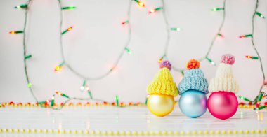 Beyaz arka planda Noel süsleri ve çelenkler. Kardan adam şeklinde bir kepte üç renkli balon. Noel kompozisyonu.