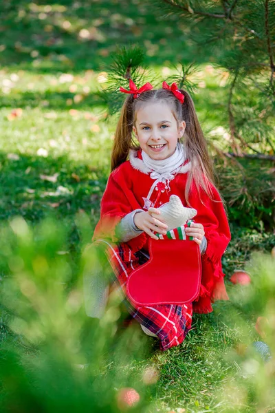 Portrait of a little girl near the Christmas tree. Girl decorates a Christmas tree in the forest with Christmas balls. — Stock Photo, Image