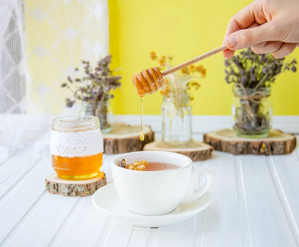 White cup of tea with linden in natural organic herbs and a jar of honey on a white wooden table. — Stock Photo, Image