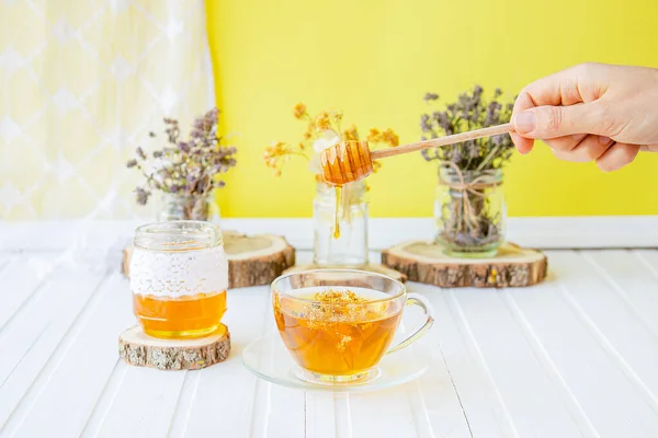 Glass cup of tea with linden in natural organic herbs and a jar of honey on a white wooden table. — Stock Photo, Image