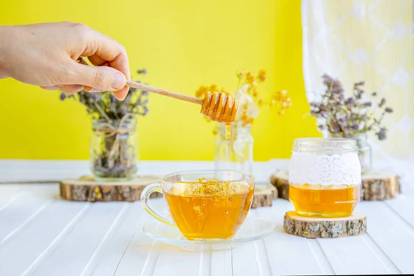 Glass cup of tea with linden in natural organic herbs and a jar of honey on a white wooden table. — Stock Photo, Image