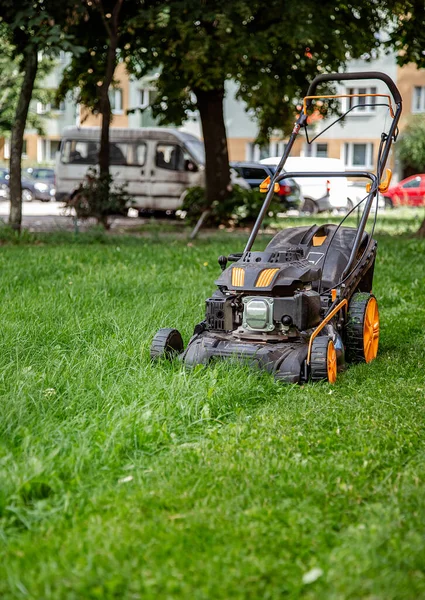 Der Arbeiter mäht das Gras auf der Baustelle, pflegt den Garten, benutzt einen Benzin-Rasenmäher. — Stockfoto