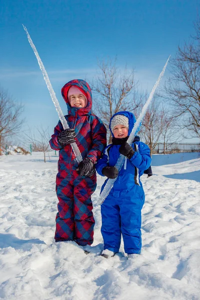 Happy brother and sister play on a winter walk, making snowballs in the park. Winter outdoor games.