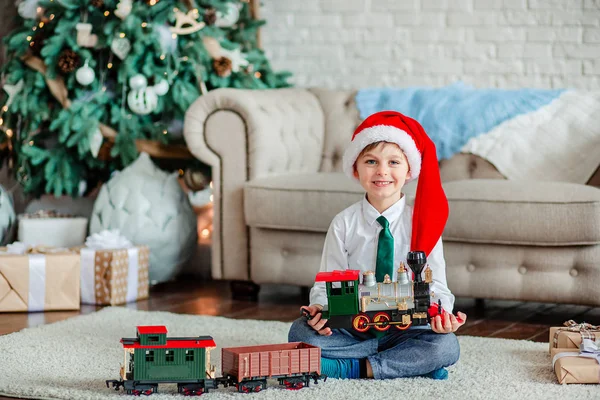 Bonjour. Bonjour. Joyeux petit garçon avec un cadeau, train jouet, sous le sapin de Noël le matin du Nouvel An. Temps pour réaliser les souhaits . — Photo