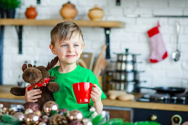 Bonjour. Bonjour. Un petit garçon boit du thé à la table de la cuisine et étreint un orignal en peluche. Un temps de miracles et d'accomplissement des désirs . — Photo