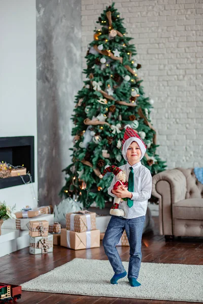 Mignon un garçon déballer des cadeaux sous le sapin de Noël, assis près de la cheminée, le matin de Noël . — Photo