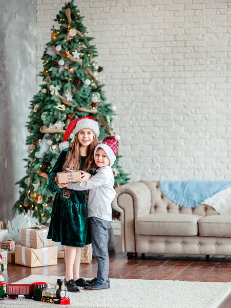 Frère et sœur donnent et déballer des cadeaux sous le sapin de Noël, assis près de la cheminée, le matin de Noël . — Photo