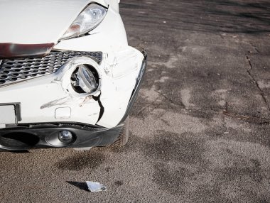 Araba kazası ya da kaza. Ön kanat ve sağ far kırılmış, tamponda hasar ve çizikler var. Kırık araba parçaları ya da yakın çekim.