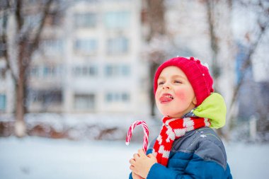 Bir kış sokağında elinde Noel lolipopu olan neşeli bir çocuğun portresi.