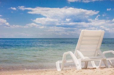 Plajın kumsalında denize karşı duran küçük plastik bir sandalye..