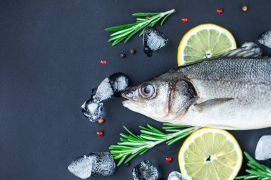 Taze levrek. Çiğ balık levreği, baharatlar ve siyah tahta üzerinde bitkiler..