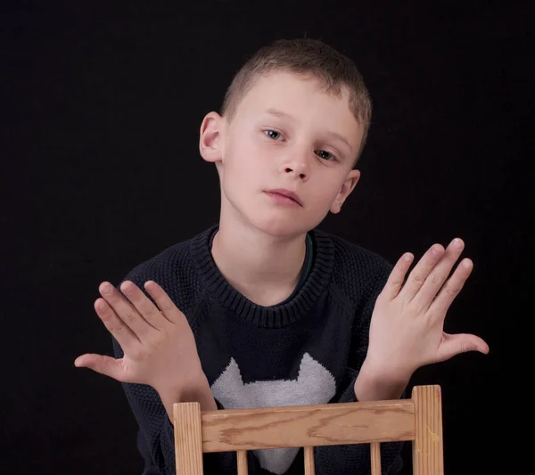 Rapaz senta-se na cadeira e levanta os braços — Fotografia de Stock