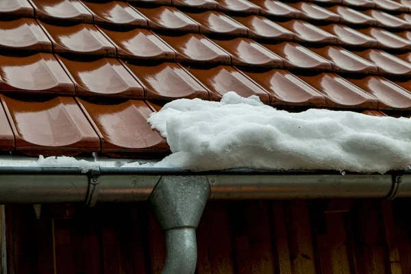 Red roof tiles with snow and gutters