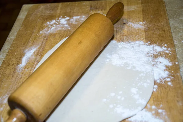 Ciasto pizzowe okrągłe jest zwijane z mąką i deską drewnianą — Zdjęcie stockowe