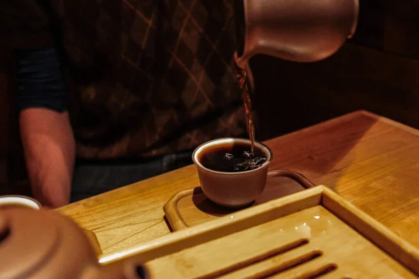 Despejando chá pu-erh escuro de um frasco de barro roxo em uma pequena xícara de degustação — Fotografia de Stock