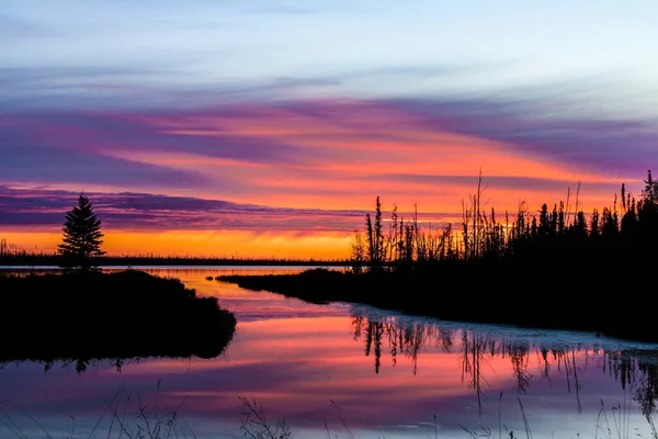 Orange, purple and grey sunset with forest inlet silhouette and reflections — Stockfoto