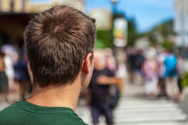 Yeşil gömlekli genç adam caddeyi geçmeden önce ileriye bakıyor.