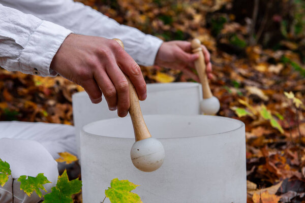 Молодой человек играет на двух хрустальных чашах в лесу - боковой вид
