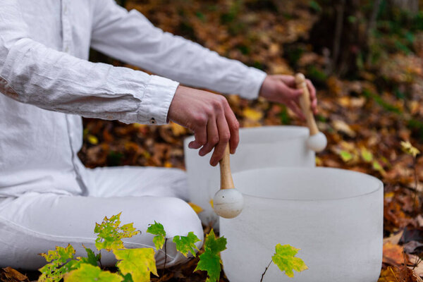 Молодой человек играет на двух хрустальных чашах в лесу - боковой вид, широкий угол
