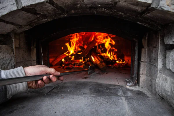 Pekárna na chleba s ohněm uvnitř, zatímco člověk hýbe dřevem s nářadím — Stock fotografie
