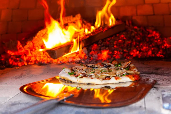 El hombre está poniendo una pizza recién preparada en un horno de pan al aire libre  - — Foto de Stock