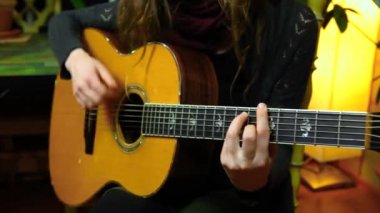 Kız evde akustik gitar çalıyor.