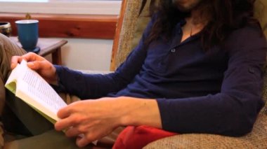 Adam oturma odasında kitap okuyor.
