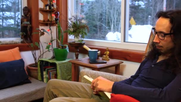 El hombre está leyendo un libro en su salón — Vídeos de Stock