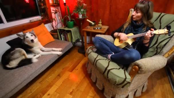 Flicka spelar ukulele i vardagsrummet. — Stockvideo