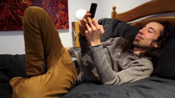 Mannen på sin mobiltelefon i sängen. — Stockvideo