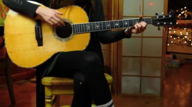 Kız evde akustik gitar çalıyor.