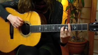 Kız evde akustik gitar çalıyor.
