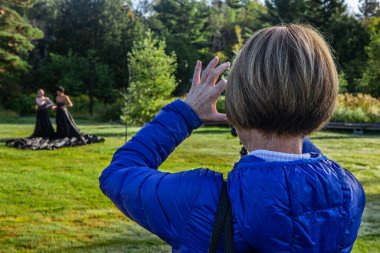 Sanatsal yoga yapan bir çifti izleyen bir kadın.