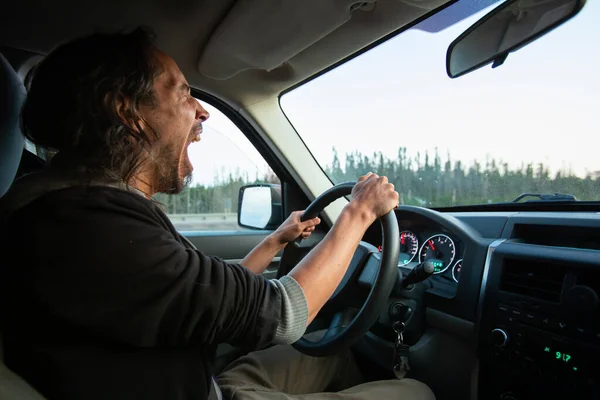 Человек устало зевает за рулём своей машины — стоковое фото