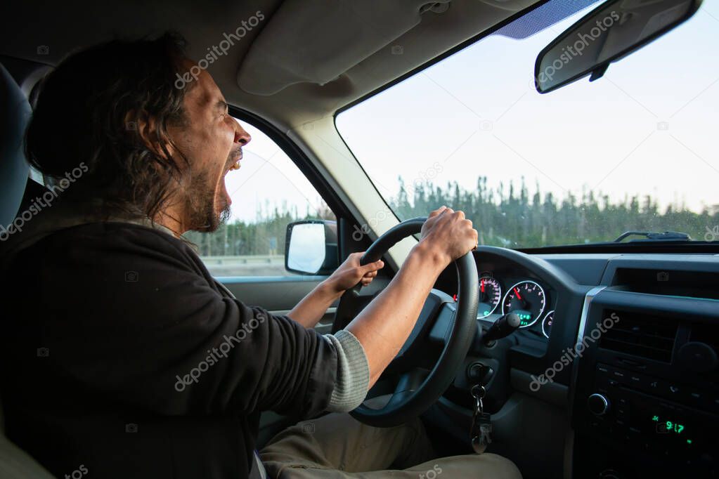 Man tiredly yawning while driving his car