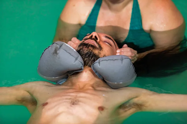 Therapist doing facial massage to man in pool — Stock Photo, Image