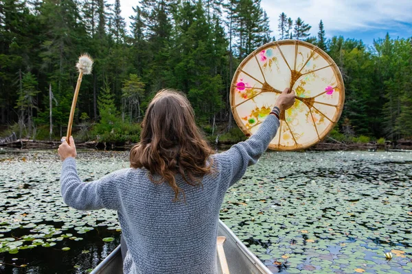 Woman holding sacred drum and stick in canoe — 스톡 사진