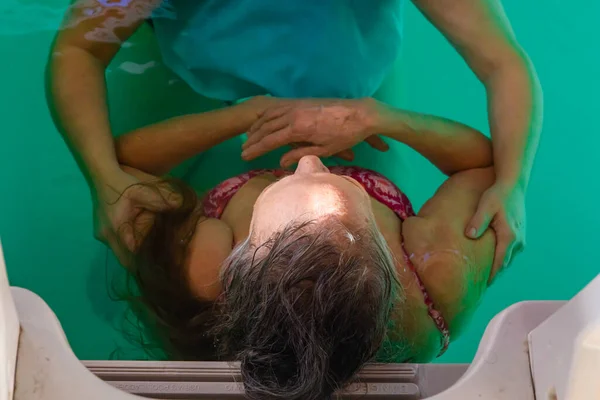 Старшая женщина принимает массаж тела в бассейне — стоковое фото